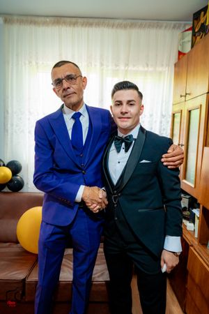 Two people in contrasting blue and black suits shake hands in a room with balloons.