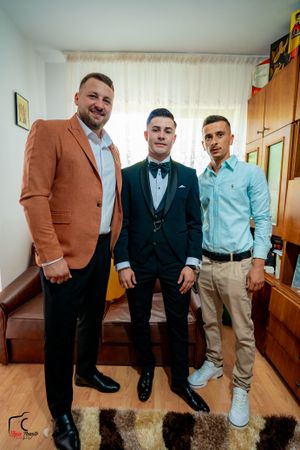 Groomsmen in brown blazers and blue shirts pose playfully in a hallway before a wedding celebration.