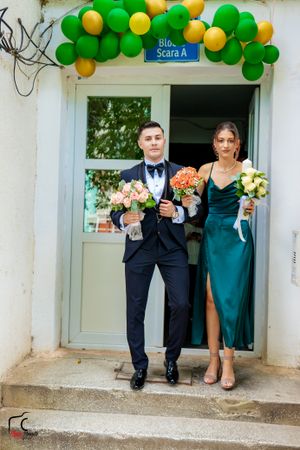 Wedding party members exit building decorated with green and yellow balloon arch.