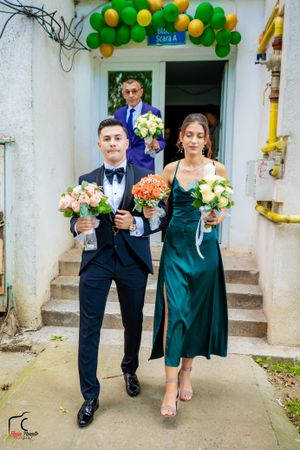 Wedding party members in formal attire walking under green and yellow balloon decorations.