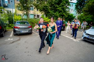 Wedding celebration group walking outdoors near parked cars and apartment buildings.