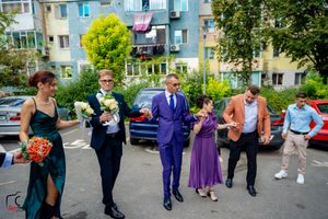 Wedding party and guests celebrating outside an apartment complex on a sunny day.