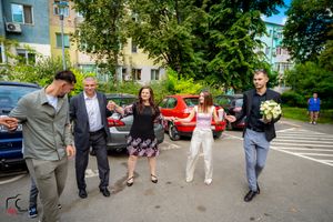 Wedding celebration with guests socializing in a parking lot surrounded by trees and buildings.