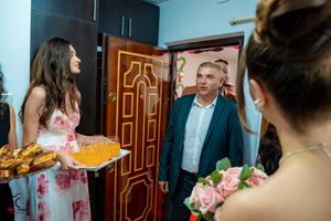 Wedding guests in formal attire gather around a doorway with refreshments and flowers.