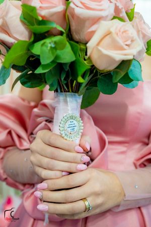Delicate pink roses in a decorated vase held by hands with manicured nails and rings.
