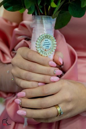 Close-up of hands holding a bouquet with an ornate vase decoration and pink nail polish.