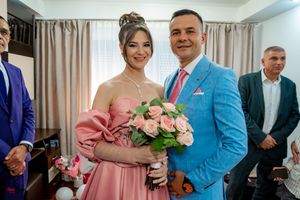 A couple in formal attire, with her wearing a pink off-shoulder dress and holding a bouquet of roses.