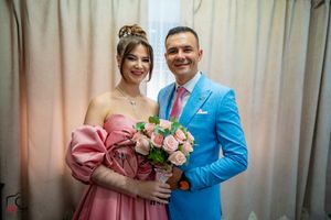A formal portrait of a couple in coordinating pink and blue outfits with roses.
