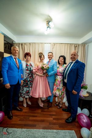 A group poses together in formal attire including blue suits and floral dresses at an indoor celebration.