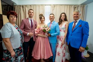 Wedding party members line up for photos in a room with cream curtains and hardwood floors.