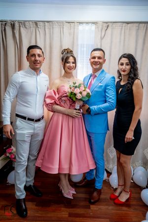 Group photo showing celebration attendees in coordinated white, pink, and blue formal outfits.