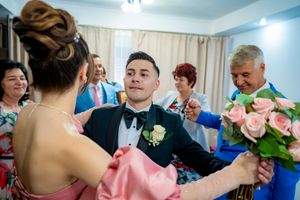 Wedding party members celebrate in a room with pink floral accents and white curtains.