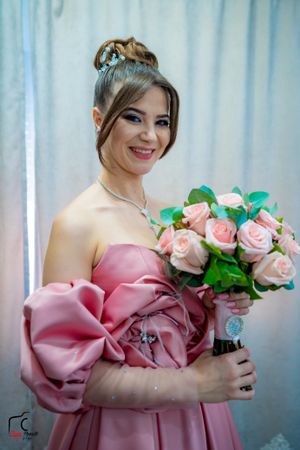 A pink satin dress adorned with roses creates an elegant bridal look against a white curtain backdrop.