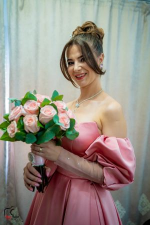 A romantic bridal portrait featuring a pink off-shoulder dress and rose bouquet.