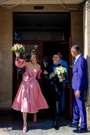 Wedding celebration outside a venue with guests in formal pink and purple attire.