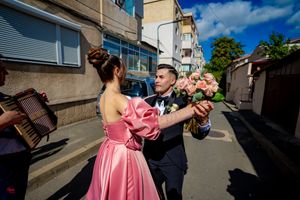 Wedding guests dancing joyfully on a sunny street with buildings in the background.