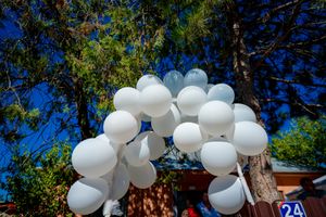 White balloons arranged in an arch formation against a bright blue sky with trees in the background.