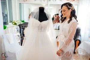 Bridesmaids in dark green dresses celebrate around a tulle wedding gown in a bright boutique setting.