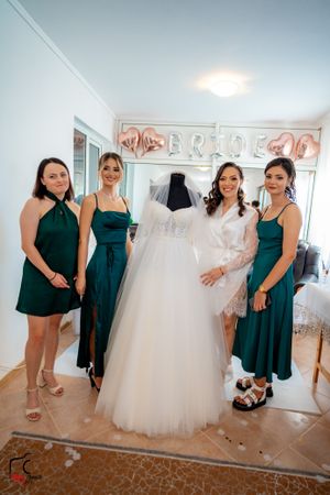 Wedding party members admire a flowing white wedding dress in a bridal shop with rose gold decor.
