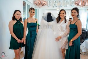Bridesmaids in matching green dresses gather excitedly around a white wedding gown display.