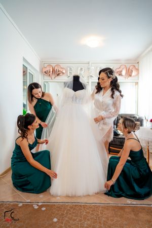 Wedding party members in emerald dresses pose playfully around a white tulle gown.