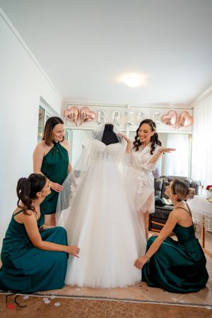 Bridesmaids share joyful moments while sitting near a displayed wedding gown.