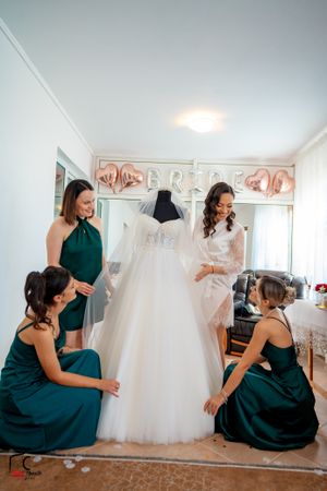 Ladies in elegant green dresses interact playfully around a white wedding dress display.