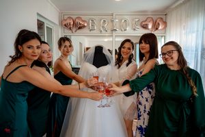 Bridesmaids in dark green dresses toast with champagne glasses during pre-wedding preparations.
