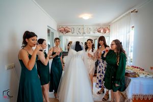 Bridesmaids wearing matching green dresses celebrate with drinks beside a displayed wedding gown.