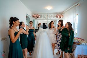 A group in coordinated green attire shares a celebratory moment in a bridal suite.