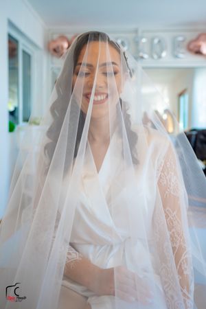 Ethereal bridal portrait through delicate white veil in natural window light.
