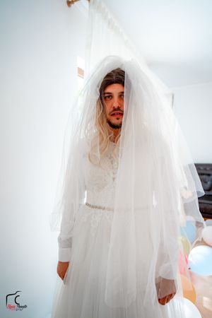 Wedding dress reveal showing flowing white gown and long veil against bright background.