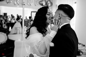 Black and white capture of a romantic wedding moment with decorative signage and guests in the background.