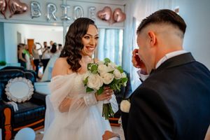 A couple shares a joyful moment during their wedding ceremony with white roses and 'BRIDE' decor in the background.