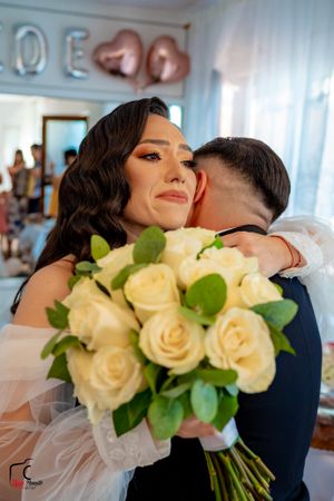 An emotional embrace during a wedding ceremony with cream roses and heart decorations in the background.