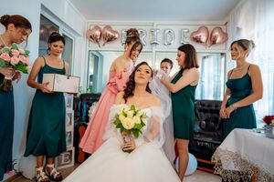 Wedding party gathered in a bright room with bridesmaids in teal dresses and pink accents.