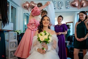 Candid wedding preparation scene with bridesmaids in colorful dresses against white walls.