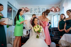 Wedding preparation scene with bridesmaids in pink and purple dresses helping with final touches.