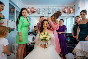 Bridal party getting ready in a room with silver 'BRIDE' balloon letters on the wall.