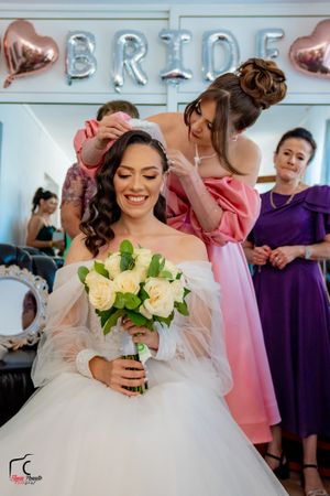 Bride in white ballgown holding yellow bouquet surrounded by bridesmaids in colorful dresses.