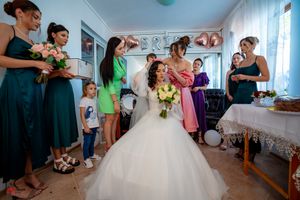 Getting ready scene with bride in white gown surrounded by bridesmaids in pink and purple dresses.