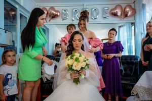 Bride in white ballgown dress holding yellow bouquet with bridesmaids in colorful attire nearby.
