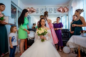 Wedding party gathers in a bright room with bridesmaids wearing colorful dresses in pink, green and purple tones.
