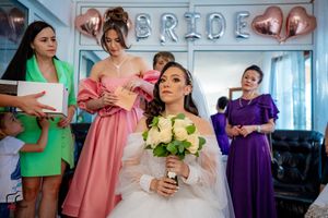 Wedding party members in coordinated dresses of pink, green and purple gather around a white-gowned bride.