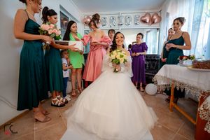 Bridal party in pastel dresses assembles in a light-filled room with decorative wall details.