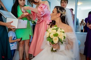 Wedding party members in coordinated pastel dresses help prepare in a bright indoor setting.