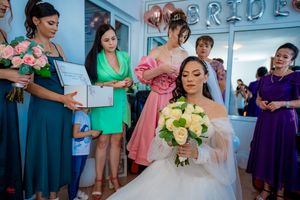 Bridal party wearing mix of pink, green and purple dresses gathered in preparation room.
