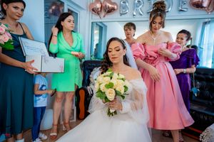 Pre-wedding scene with bridal party wearing mix of pink, green and purple dresses in sunlit room.