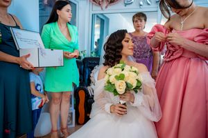 Wedding preparation moment with bridesmaids in coordinated pastel dresses helping the bride.