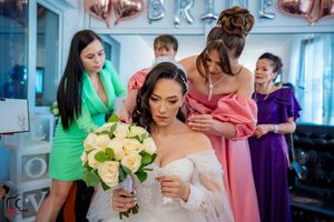 Bridal party in vibrant dresses assisting with wedding preparations in a blue-walled room.
